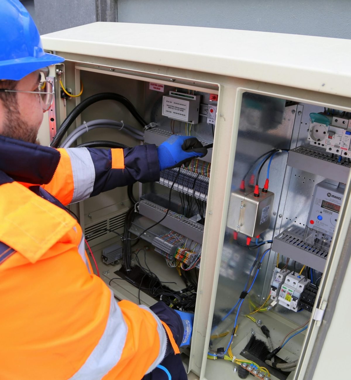 Engineer in safety gear working on an outdoor electrical panel, ensuring system functionality.